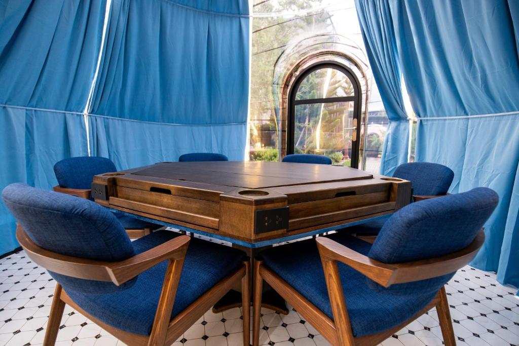 A square wooden table surrounded by blue upholstered armchairs beneath blue curtains.