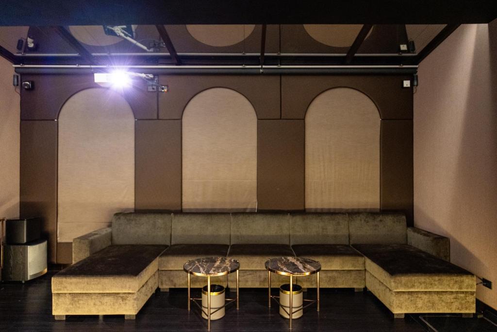 A dim, theatrical lounge with a long sectional sofa and two small round tables.