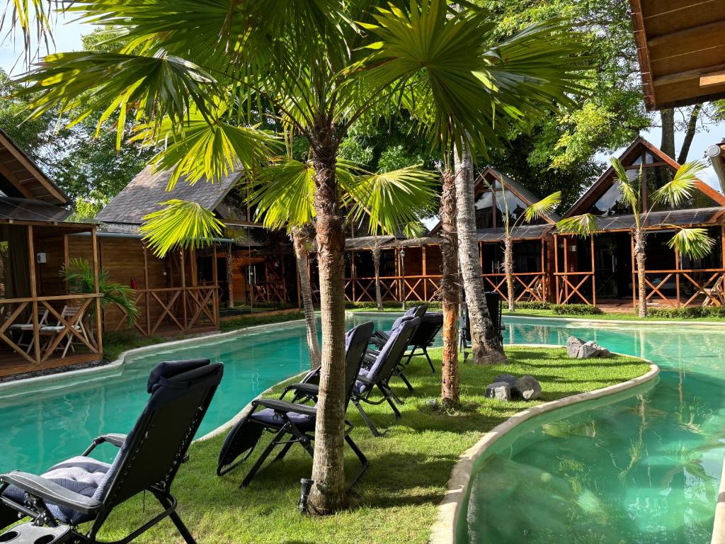 a pool with chairs and palm trees in front of a house at Lagoon Bungalows Bali in Nusa Dua