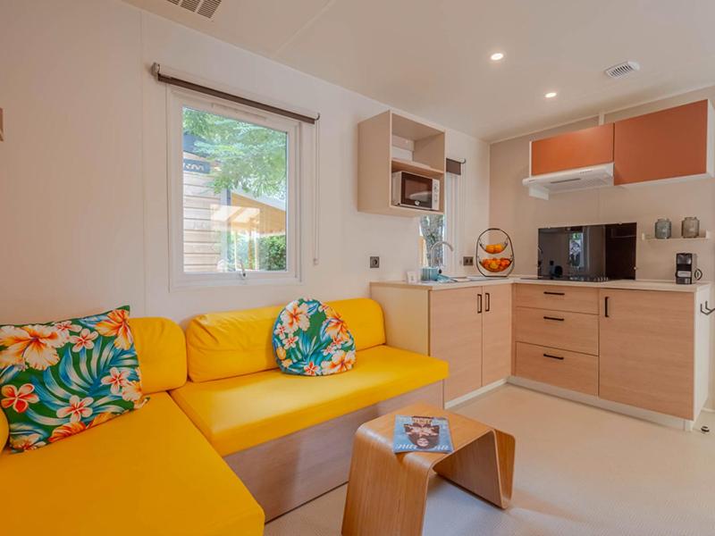 a living room with a yellow couch and a kitchen at Camping Les Grenettes in Sainte-Marie-de-Ré