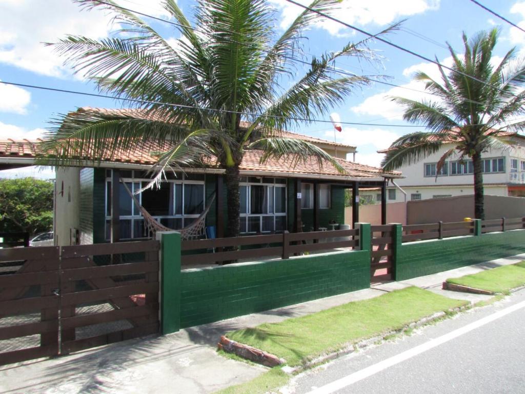 a house with a green fence and a palm tree at Saqua Beach Hostel in Saquarema