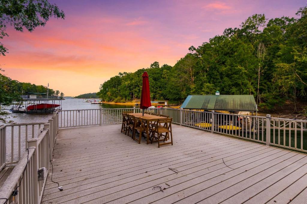 une terrasse en bois avec une table et un parasol rouge dans l'établissement 4bd Waterfront House in Lake Lanier with HotTub, FirePit, Wifi, Ping Pong and 2 Kaya, à Gainesville