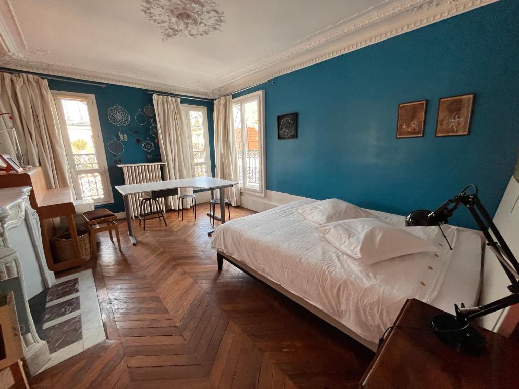 - une chambre avec des murs bleus, un lit et une table dans l'établissement Vivre au Village des Batignolles, à Paris