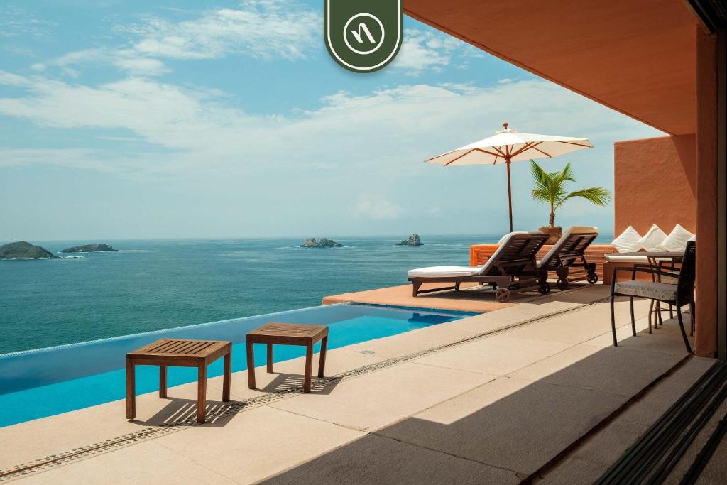 - une piscine avec des chaises et un parasol et l'océan dans l'établissement 4 BR Penthouse - Breathtaking Views - Private Pool, à Zihuatanejo