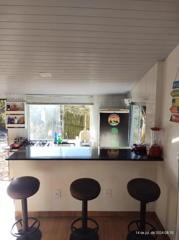 a kitchen with three bar stools in front of a counter at Chalé CIO DA TERRA in Alto Paraíso de Goiás