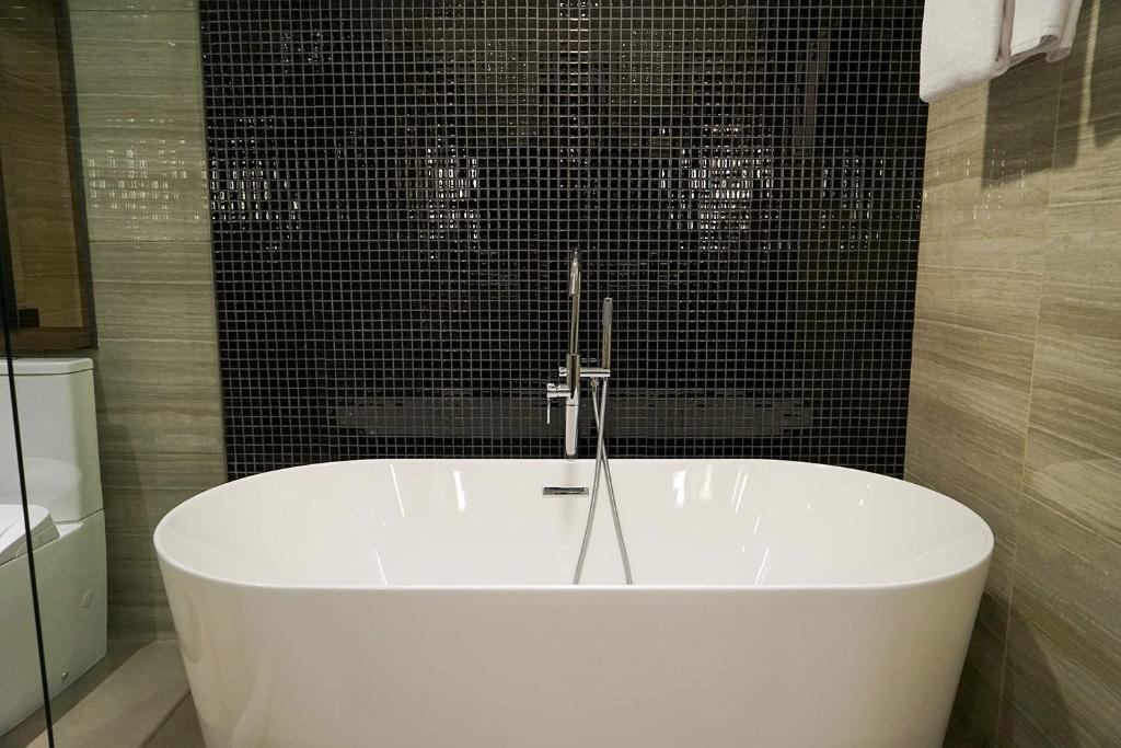 a white bath tub in a bathroom with black tiles at Swiss-Belhotel Airport Yogyakarta in Yogyakarta