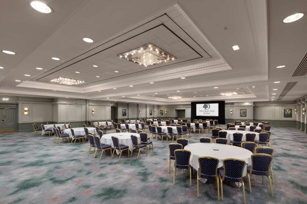 a banquet hall with tables and chairs and a screen at DoubleTree By Hilton Brighton Metropole in Brighton & Hove
