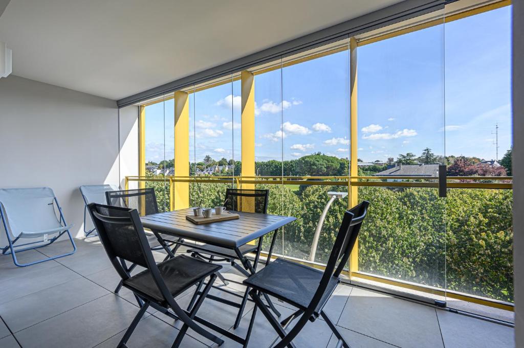 une table et des chaises dans une pièce avec une grande fenêtre dans l'établissement Les rives de la Marle - Appt avec parking couvert, à Vannes