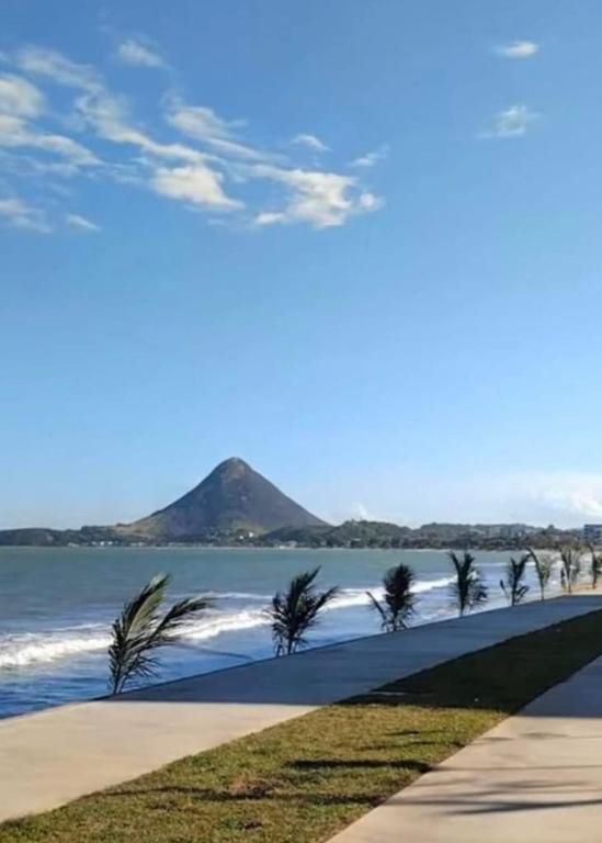 a walkway along the beach with palm trees and a mountain at Excelente apartamento em Piuma in Itapitanga