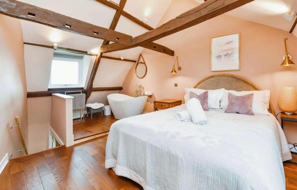 a bedroom with a large white bed and a bathroom at Rose & Star Cottage in Frome
