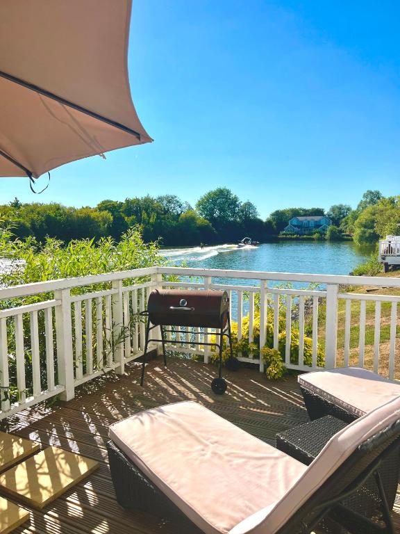 a deck with a bench and an umbrella and a river at Modern Lakefront Lodge w Deck Water Views in Cirencester