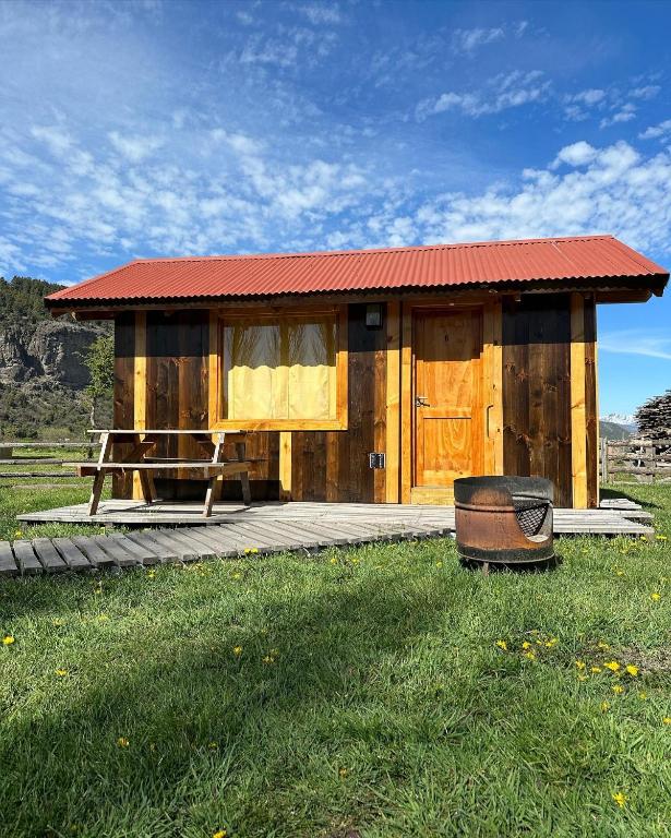 a small wooden cabin with a table and a bench at TRAVELLERS Camping & Dorms in San Martín de los Andes