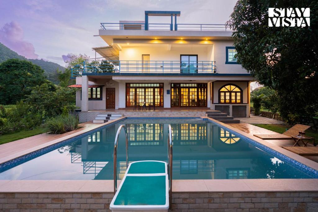a house with a swimming pool in front of it at StayVista at FarmVille with Mountain View, Pool in Alibag