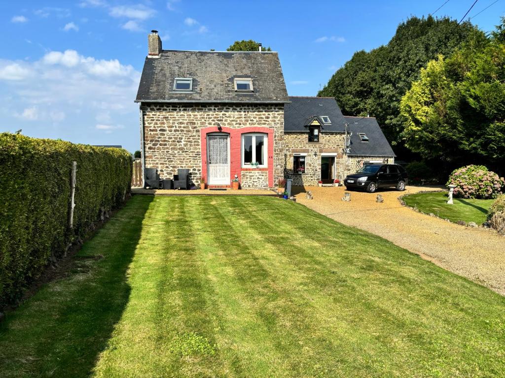 an old stone house with a red door and a yard at La Perruche Holiday Gite in Heussé