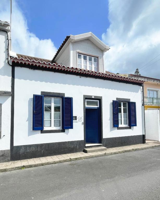 a white house with blue shutters on a street at Casa do Vale das Furnas in Furnas