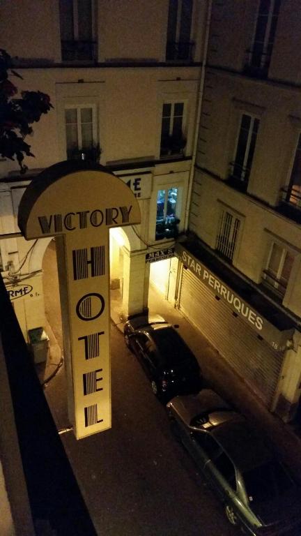 a sign in front of a building with parked cars at Victory Hotel Galou in Paris