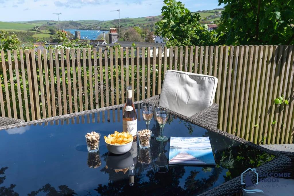 a glass table with a bottle of wine and wine glasses at The Hideout-Boutique Cabin, Estuary View & Parking in Salcombe