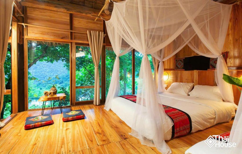 a bedroom with a bed with a canopy and a window at Thai House Pu Luong - Century Old Stilt House with Terrace Views in Hương Bá Thước