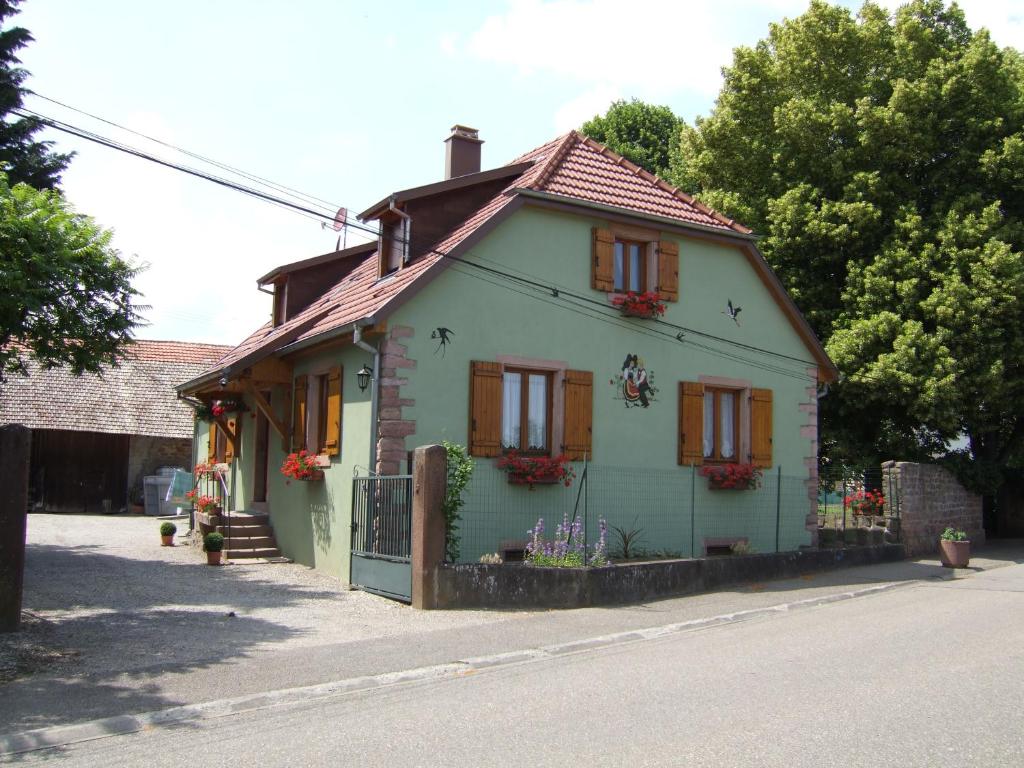 a small green house with red shutters on a street at Gîte des Hirondelles in Issenheim