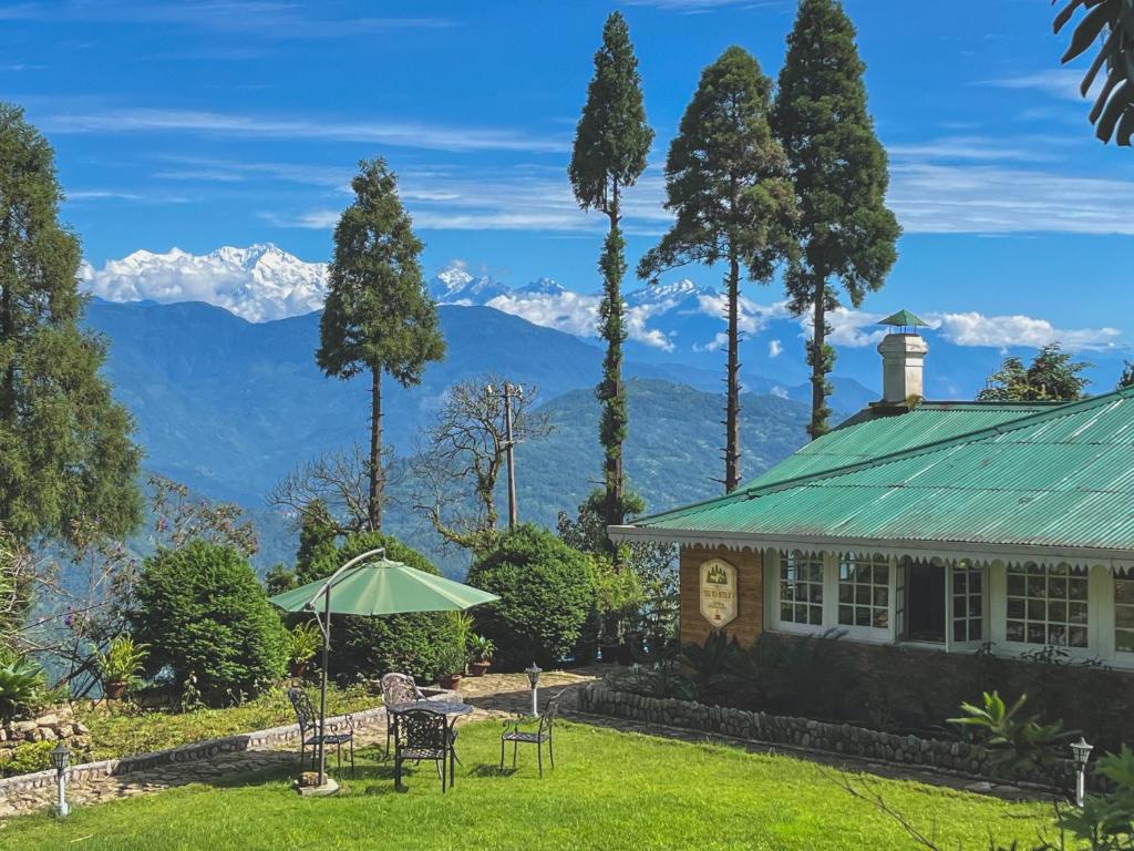 a house with a green roof with mountains in the background at Yule Tea Retreat, Darjeeling in Sukhia Pokhari