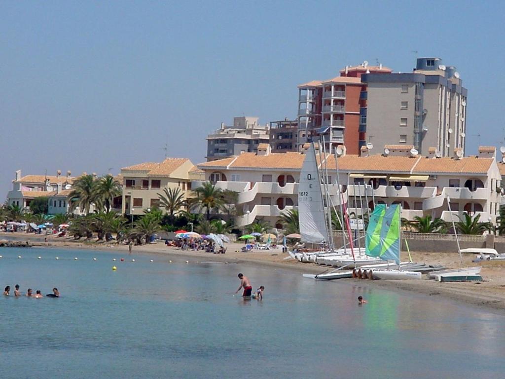 un gruppo di persone su una spiaggia con una barca a vela di Apartamentos Góndolas V.v. a La Manga del Mar Menor