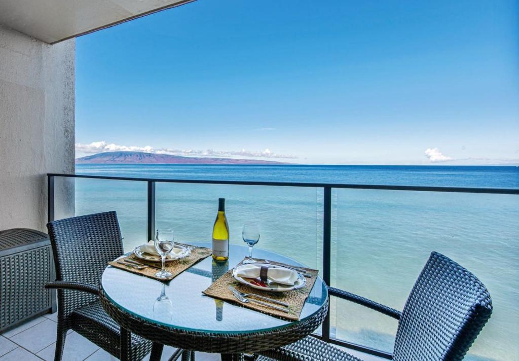 una mesa con 2 copas de vino en un balcón con vistas al océano en Mahana 803, en Kahana