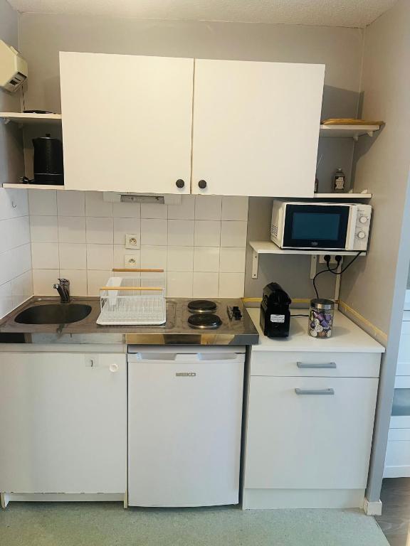 une petite cuisine avec des armoires blanches et un micro-ondes dans l'établissement Clos Guerin Saint Pierre, à Caen