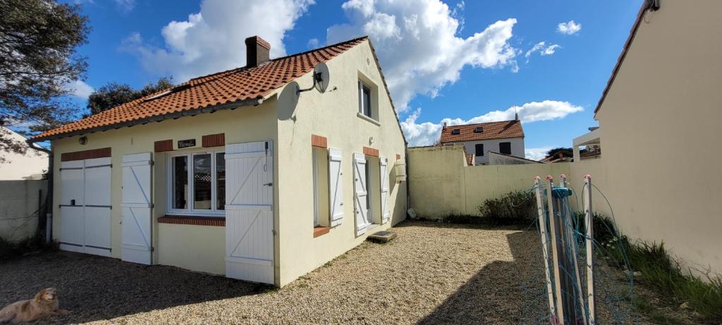 Une petite maison blanche avec un chien assis à côté dans l'établissement Gite de mer proche Pornic 6 personnes, à La Bernerie-en-Retz