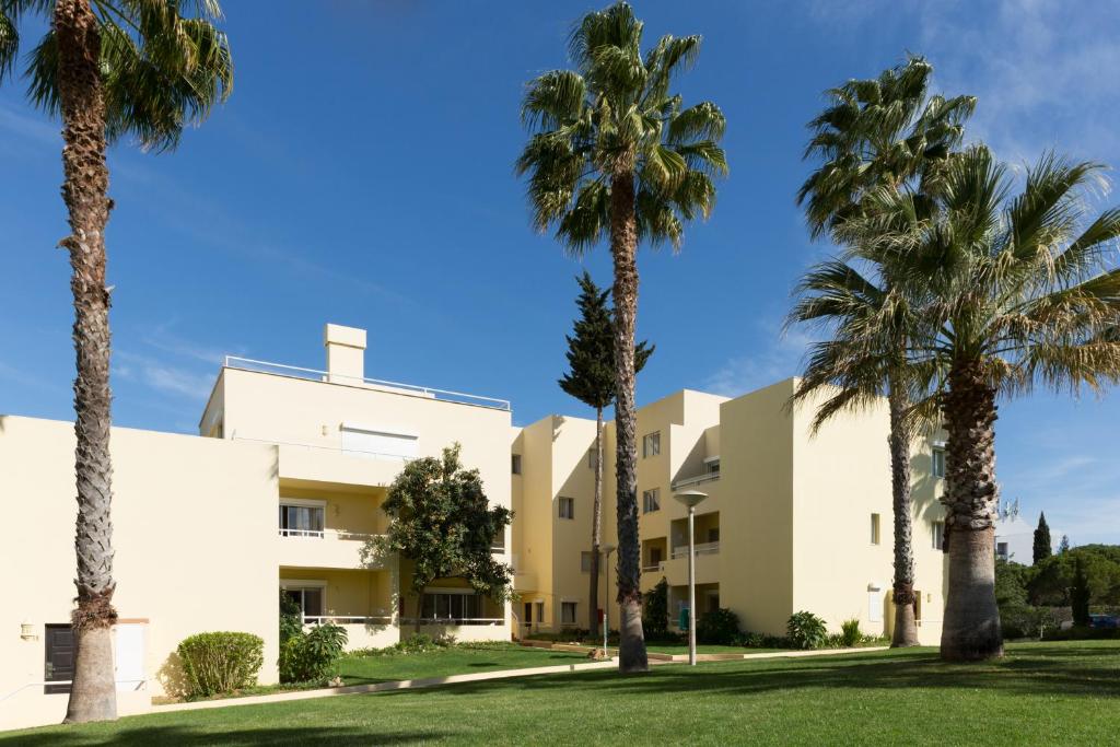 a group of palm trees in front of a building at Parque Mourabel, Oásis Village & Pé do Lago in Vilamoura