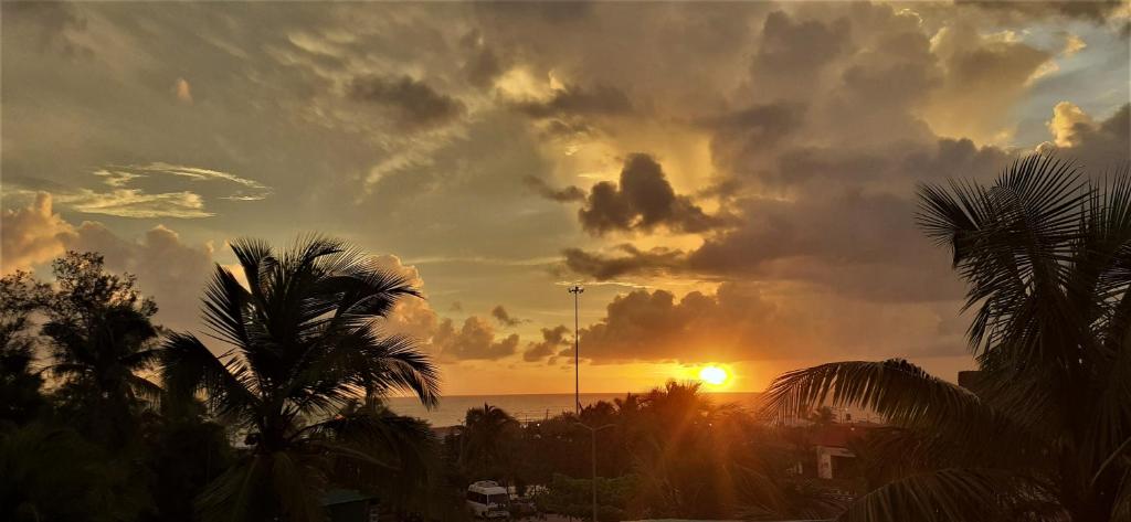 a sunset on the beach with palm trees and the ocean at Thomson by the Beach in Candolim