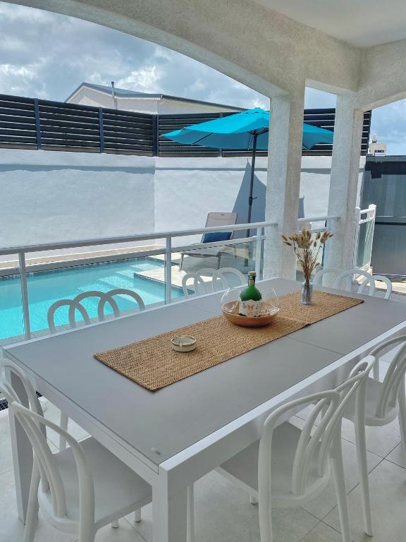 a white table and chairs on a balcony with a pool at Villa - Cosy - Piscine - Guadeloupe centre in Baie-Mahault