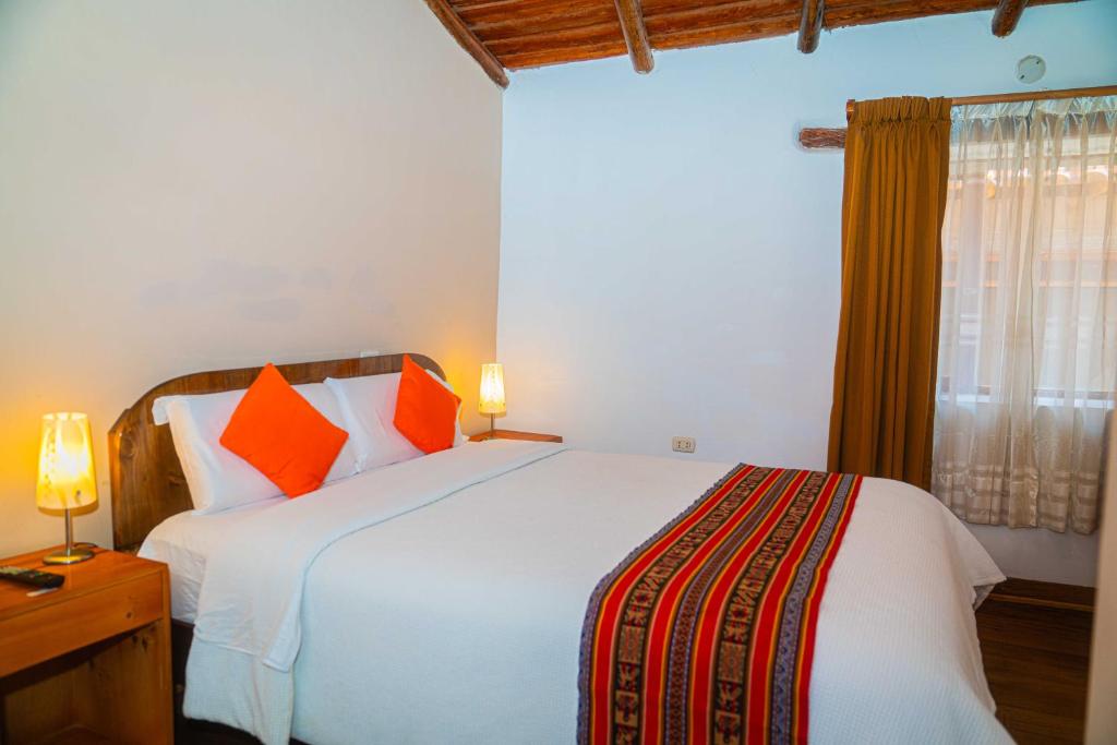 a bedroom with a large white bed with orange pillows at Casa de Ollanta ByB in Ollantaytambo