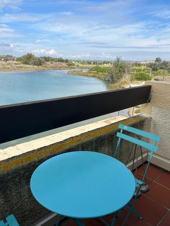 Una mesa azul en un balcón con vista a un río. en studio village naturiste, en Leucate