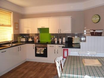 a kitchen with white cabinets and a table with a green counter top at Claremont House Holiday Apartments in Llandudno