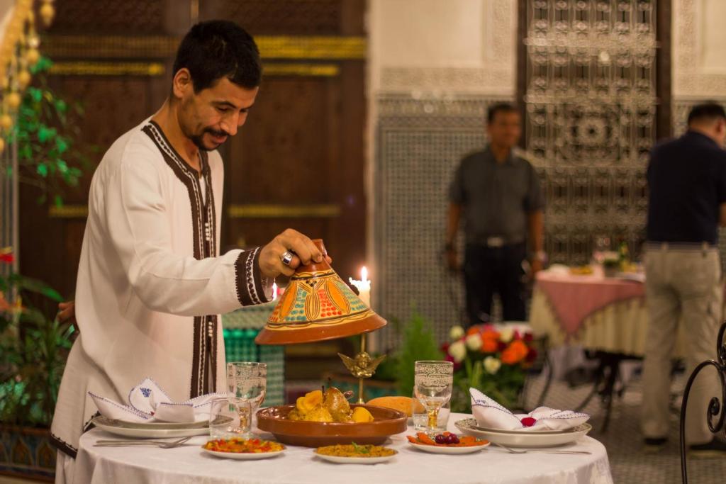 a man holding a bell over a table with food at Riad Fes Kettani in Fez