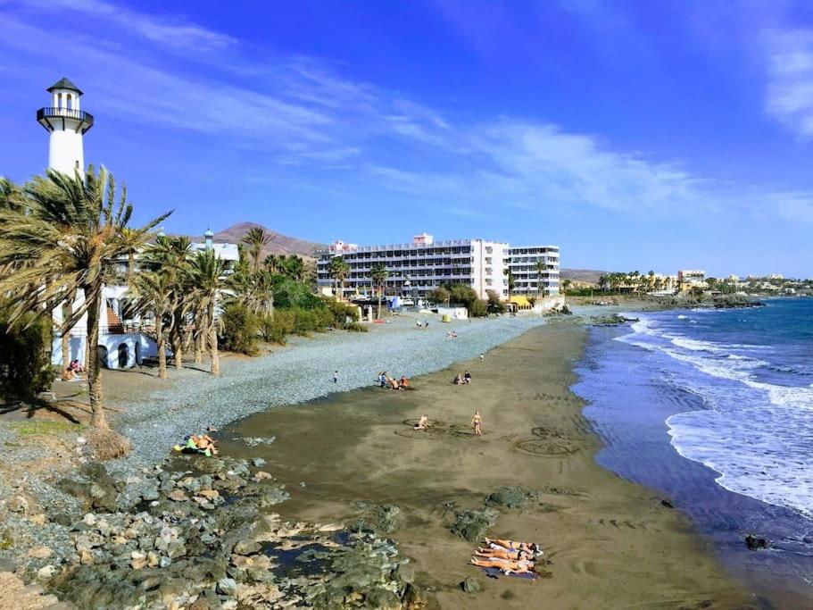 a beach with people laying on the sand and a lighthouse at Apartamento Playa Cañon del águila in Playa del Aguila