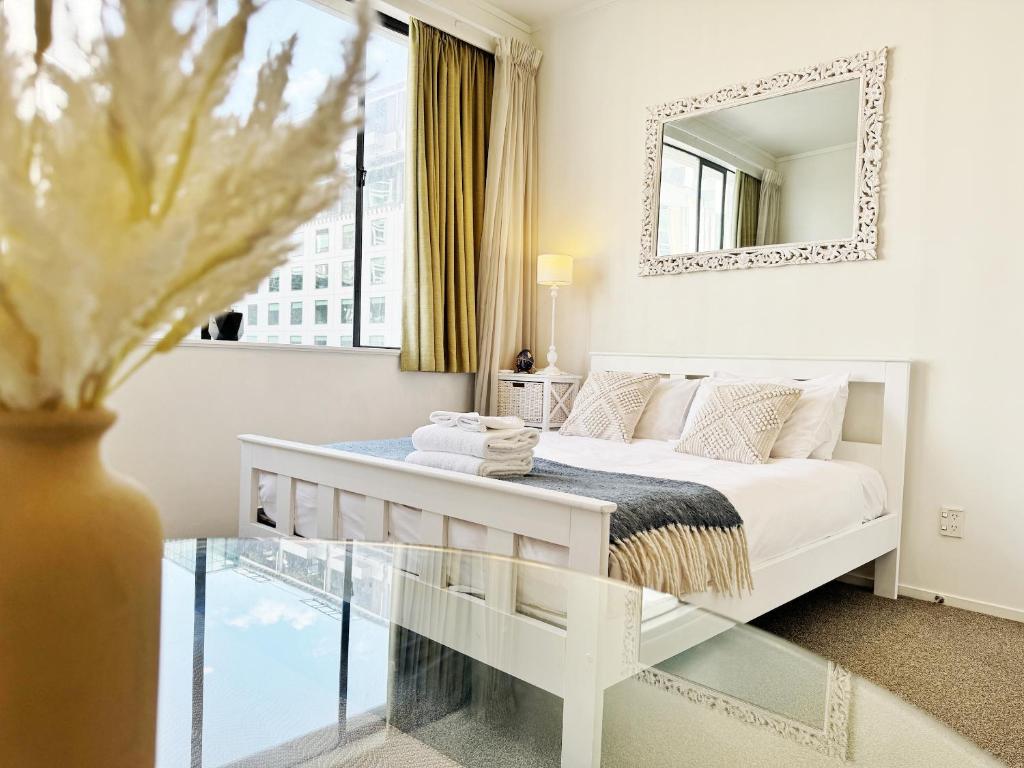 um quarto branco com uma cama e um espelho em Skytower views, washer & dryer, TV! em Auckland