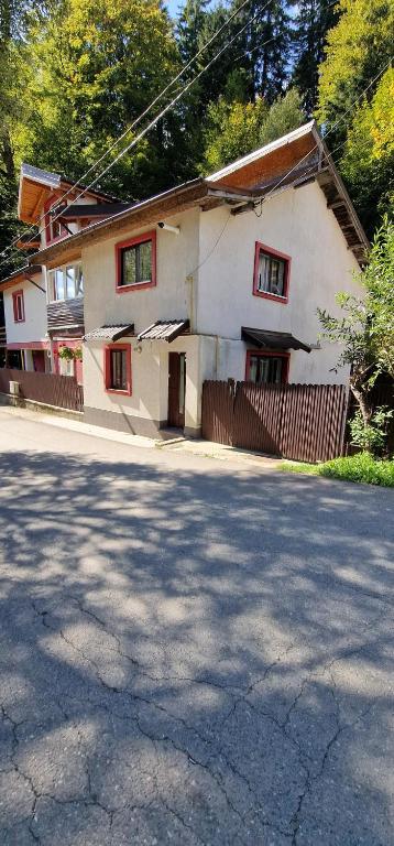 a white house with red windows on a street at Casa Kati in Buşteni