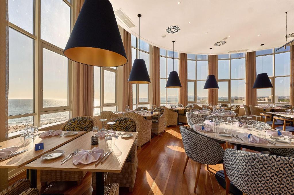 a restaurant with tables and chairs and large windows at TRYP by Wyndham Lisboa Caparica Mar in Costa da Caparica