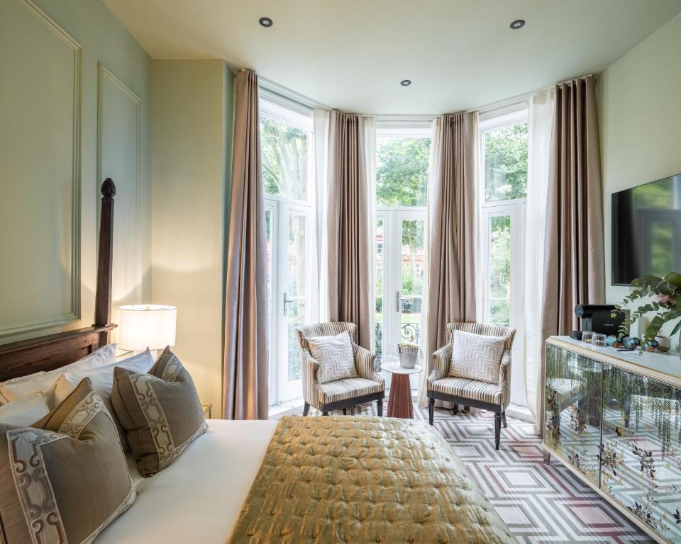 een slaapkamer met een groot bed, stoelen en ramen bij Ellen Kensington in Londen