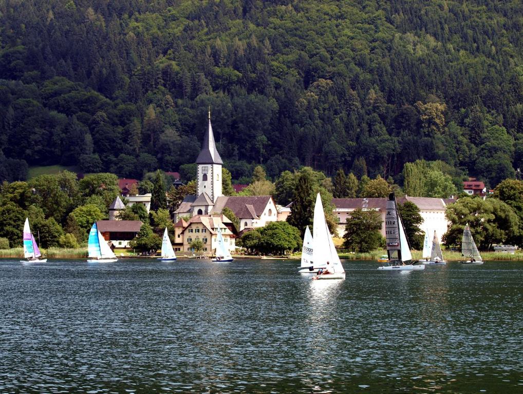 un grupo de veleros en un lago con una iglesia en Ferienwohnungen Steger en Bodensdorf