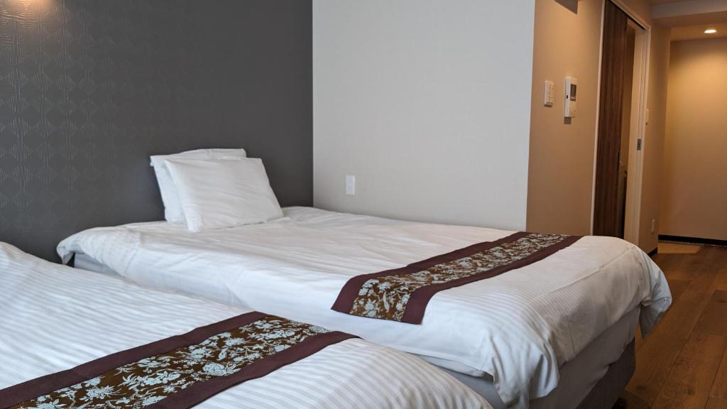 two beds in a hotel room with white sheets at Naha airport hotel in Takara