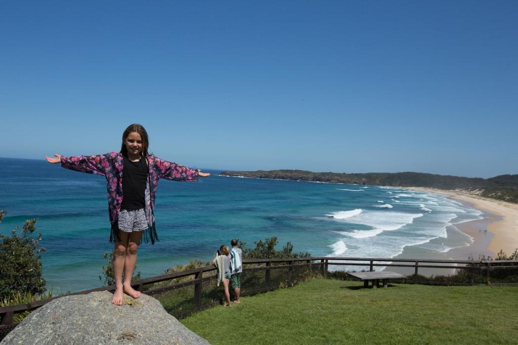 una mujer parada en la cima de una roca cerca de la playa en NRMA Myall Shores Holiday Park, en Bulahdelah