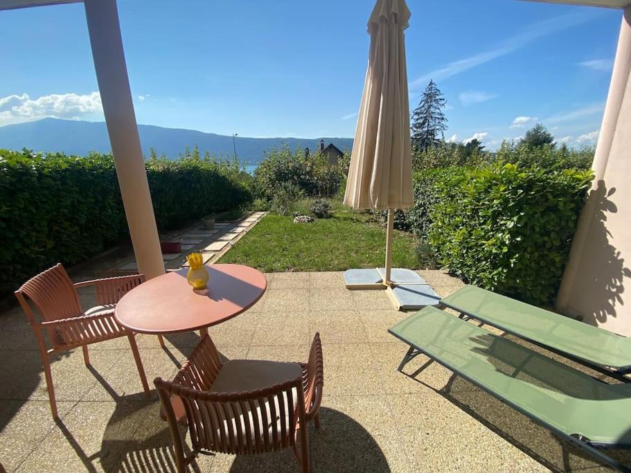 un patio avec une table, des chaises et un parasol dans l'établissement Au Bonheur des Roses, parking, terrasse & jardin, à Veyrier-du-Lac