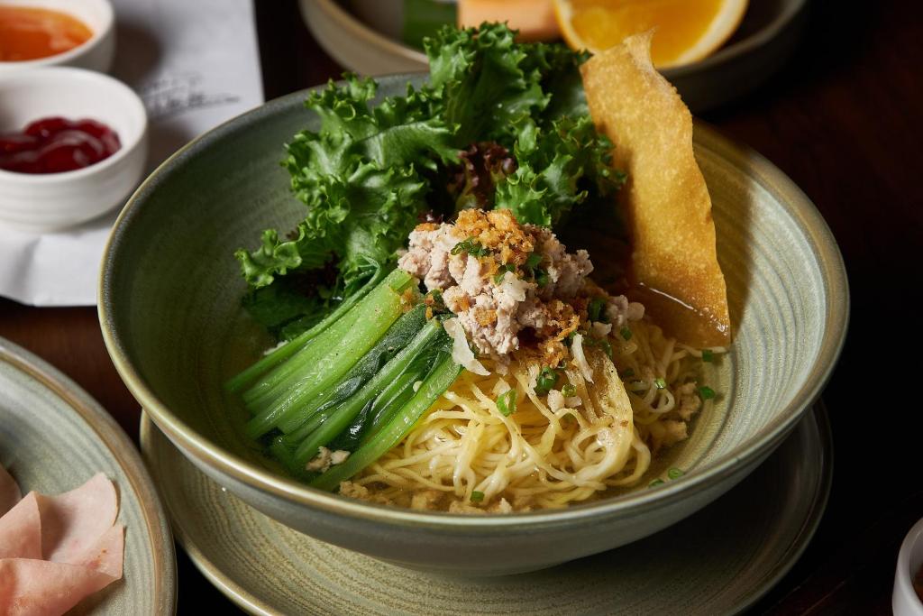 A plated noodle dish with greens, shredded topping and a crisp garnish.