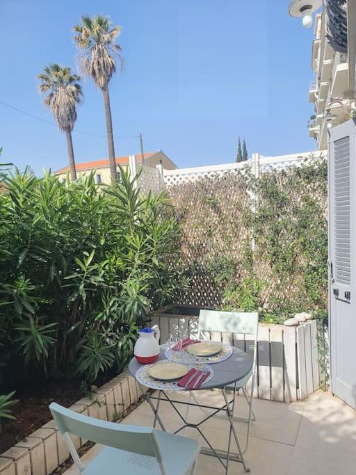 d'une terrasse avec une table, des chaises et des palmiers. dans l'établissement CANNES CALIFORNIE, WINTER PALACE, à 2 pas de la rue d'Antibes et des plages de la Croisette, à Cannes