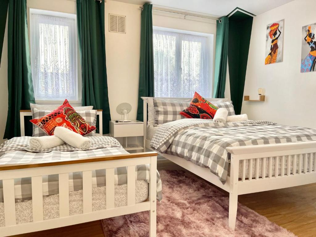 two beds in a bedroom with green curtains at The Express Apartment in Goodmayes