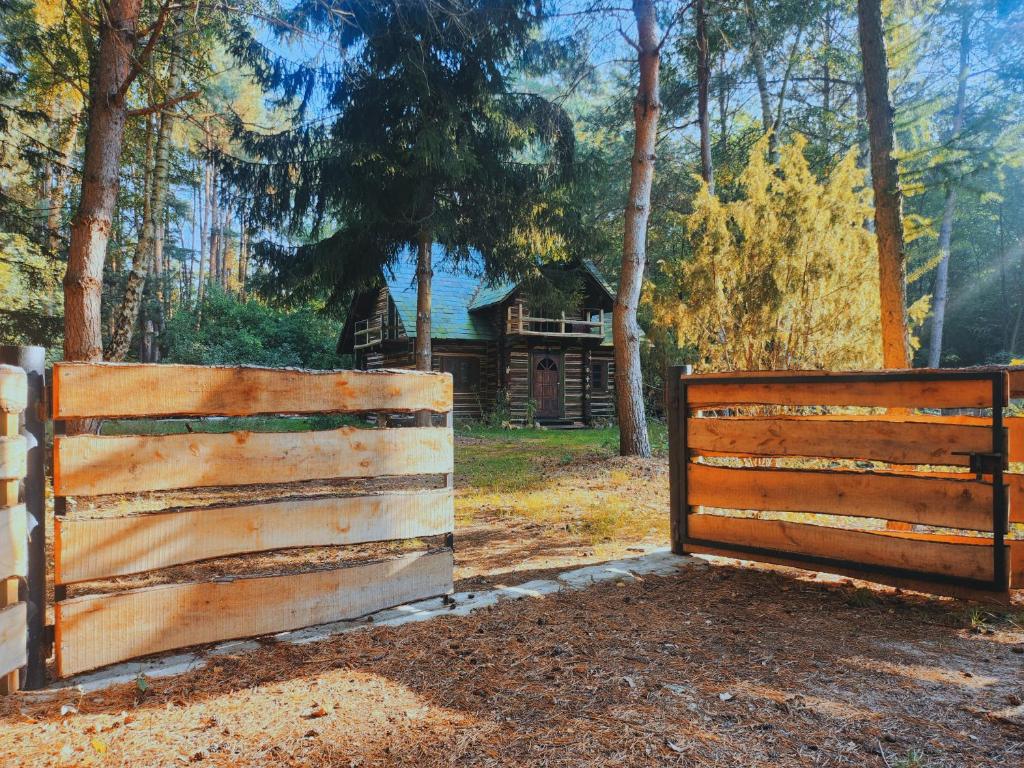 a wooden fence with a house in the background at Dzwonkarnia Wyjątkowy domek w lesie in Dzwonkowice
