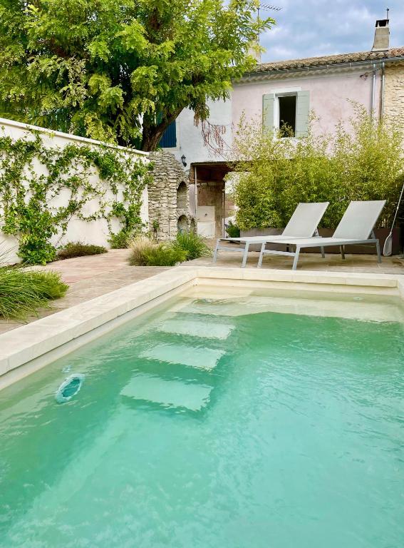 une piscine avec deux chaises blanches et une maison dans l'établissement Mazet avec piscine, parking et clim dans le centre, à Saint-Rémy-de-Provence
