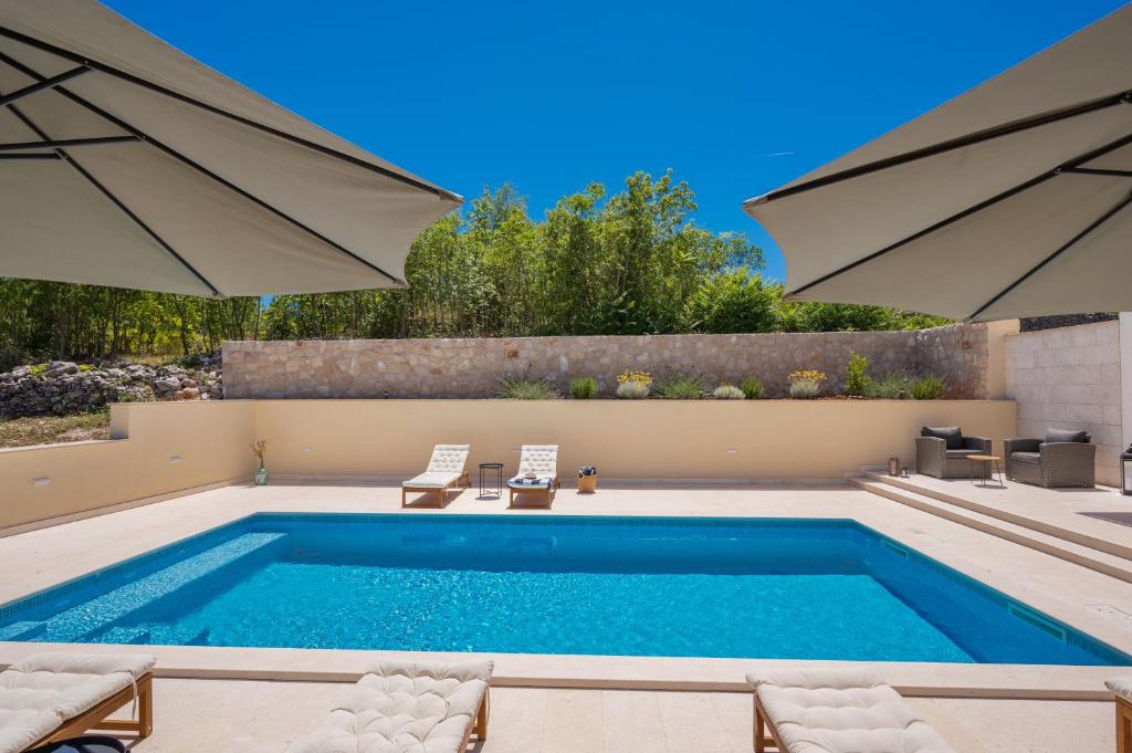 a swimming pool with two umbrellas and two chairs and a pool at Unique Villa Pietra with heated private pool in Šestanovac